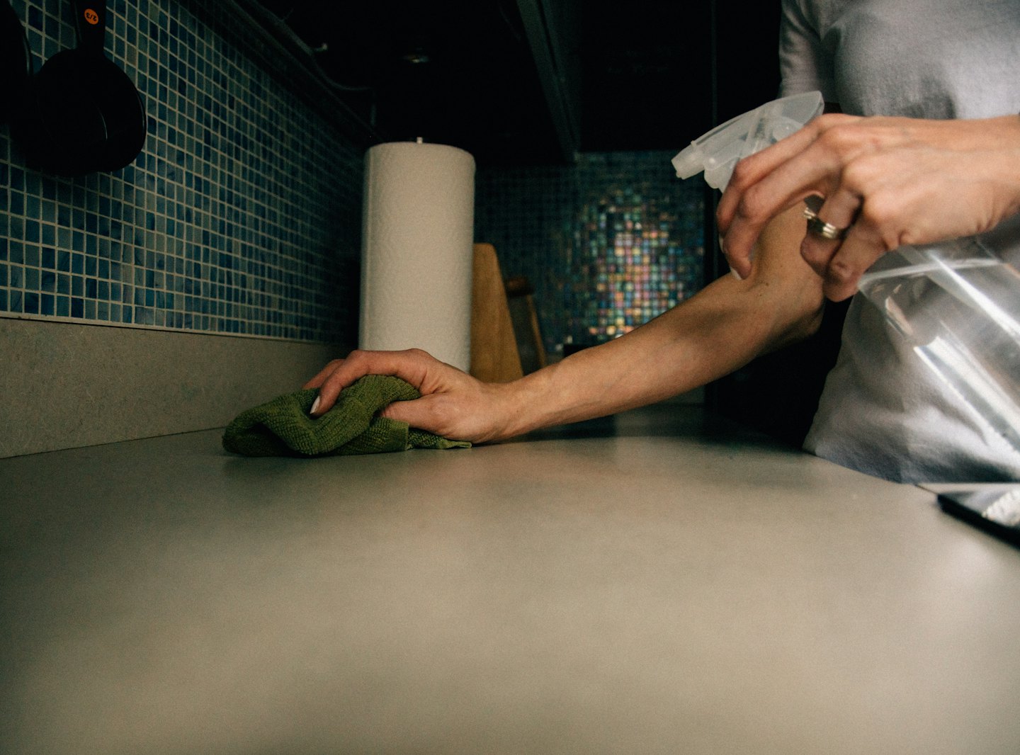 Hands cleaning a kitchen counter with a spray bottle.