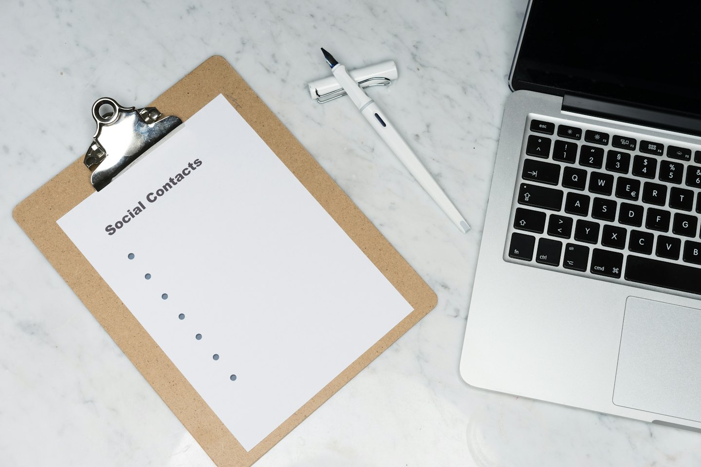 Brown clipboard, silver laptop, and white pen on a marble desk.